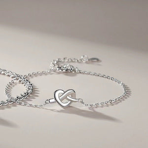 Two silver bracelets with heart-shaped knots, one with a chain link and the other with a solid pattern, placed side by side.