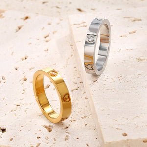 Gold and silver rings with heart and diamond designs on a textured beige surface