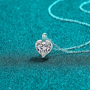 Heart-shaped silver pendant with clear gemstone on a turquoise background
