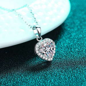 Heart-shaped diamond pendant on a chain against a teal background