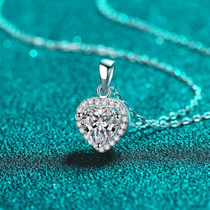 Heart-shaped silver pendant with clear gemstone on a turquoise background