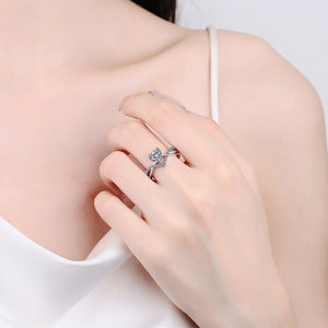 Close-up of a hand wearing a silver ring with a bow design on a light background