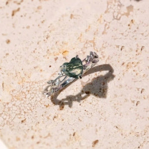 Silver ring with green gemstone on a beige stone surface