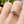 Heart-shaped green gemstone ring on a finger with a blurred natural background