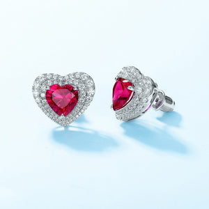 Heart-shaped ruby earrings with diamond accents on a light blue background