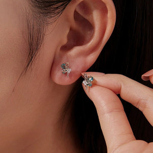 Close-up of a person wearing butterfly-shaped earrings with gemstones.