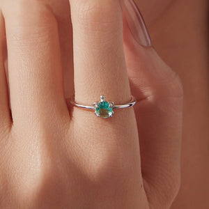 Silver sea turtle ring with a blue gemstone on a person's finger against a neutral background