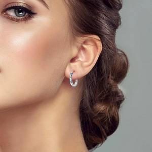 Close-up of a woman wearing silver butterfly hoop earrings with a gray background