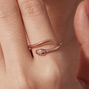 Rose gold snake-shaped ring on a finger with a soft focus background