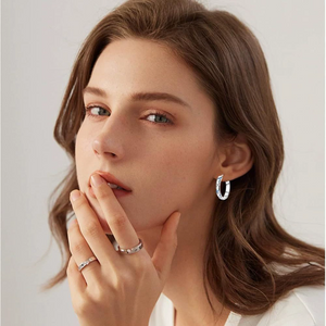 Close-up of a woman wearing silver butterfly hoop earrings with a gray background