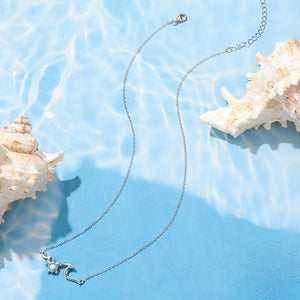 Silver necklace with a sea turtle and wave pendant on a blue surface with shells.