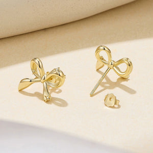 Gold bow-shaped earrings on a beige background