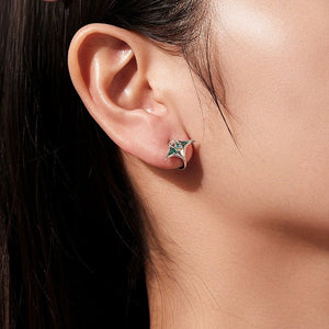 Close-up of an ear wearing a silver manta ray earring with a green gemstone.