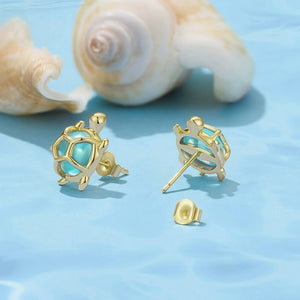 Gold sea turtle earrings with blue cubic zirconia on a blue background with shells.