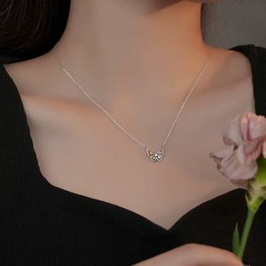Woman wearing a butterfly-shaped necklace with colorful gemstones on a gray background