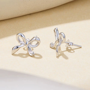 Silver bow-shaped earrings on a beige background