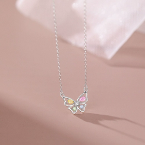 Butterfly-shaped necklace with colorful gemstones on a soft pink background
