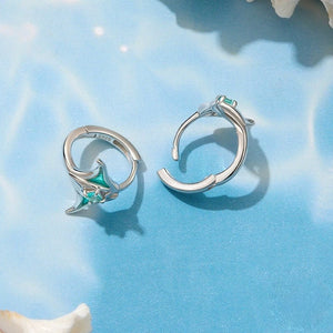 Silver manta ray hoop earrings with green gemstones on a blue background