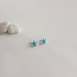Blue starfish-shaped earrings on a light gray surface with white stones.