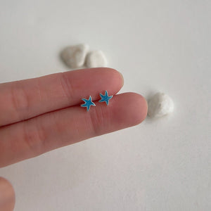 Small blue starfish earrings held between fingers on a light background