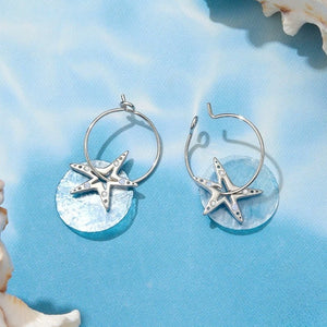 Silver hoop earrings with starfish charms on a blue shell background