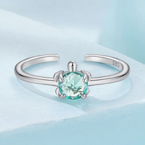Silver sea turtle ring with a blue gemstone on a light blue background