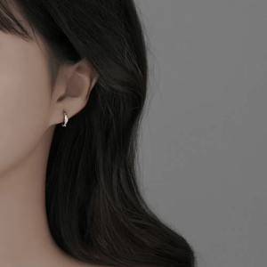 Close-up of an ear wearing a diamond earring with dark hair and a neutral background