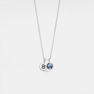 A white gold-plated sterling silver necklace with a small circular charm featuring a letter 'A' and a crystal glass projection bead inset.