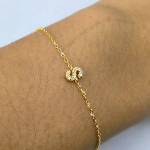 Gold bracelet with a heart-shaped clasp on a wrist against a light background