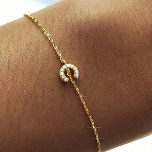 Gold bracelet with a circular diamond pendant on a wrist.
