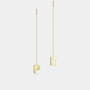 Gold earrings with 'P' and 'E' charms on a light gray background
