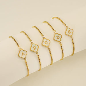 Gold bracelets with letter charms on a beige background