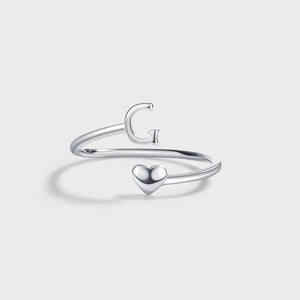A set of three sterling silver stacking rings with bypass design, each ring with a different letter initial: R, U, and A, displayed on a white plate with dried flowers beside them.