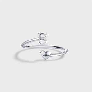 A set of three sterling silver stacking rings with bypass design, each ring with a different letter initial: R, U, and A, displayed on a white plate with dried flowers beside them.