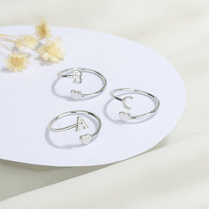Three silver rings with letters on a white plate with dried flowers.