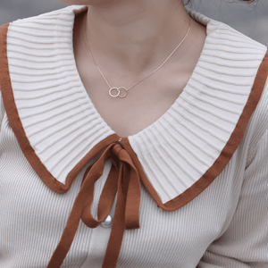 Close-up of a person wearing a beige sweater with a brown collar and a gold necklace with interlocking rings.