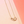Gold necklace with a rectangular pendant on a pink background