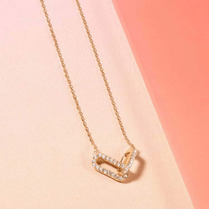 Gold necklace with a rectangular pendant on a pink background