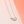 Silver necklace with a rectangular pendant on a pink background