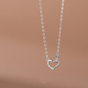 Two heart-shaped pendant necklaces, one in silver and one in gold plating, attached to chains, displayed against a neutral background.