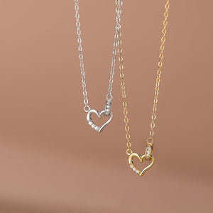 Two heart-shaped pendants on gold and silver chains against a brown background