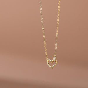 Two heart-shaped pendant necklaces, one in silver and one in gold plating, attached to chains, displayed against a neutral background.
