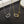 Two necklaces, one gold and one silver, with geometric pendants on a dark textured surface.