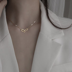 Two interlocking rectangle pendant necklaces, one plated in silver and the other in gold, set against a dark background.