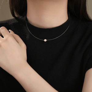 Person wearing a delicate necklace with a pearl pendant on a plain background
