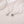 Two silver necklaces with gemstone pendants on a light pink surface
