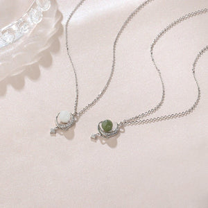 Two silver necklaces with gemstone pendants on a light pink surface