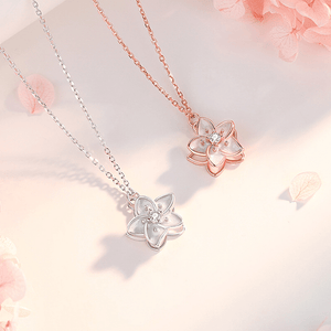 Two floral necklaces, one silver and one rose gold, on a soft pink background.
