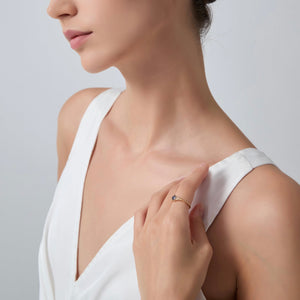 Woman wearing a white dress with a gold ring on her finger against a gray background