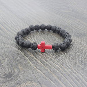 Black beaded bracelet with a pink cross charm on a wooden surface